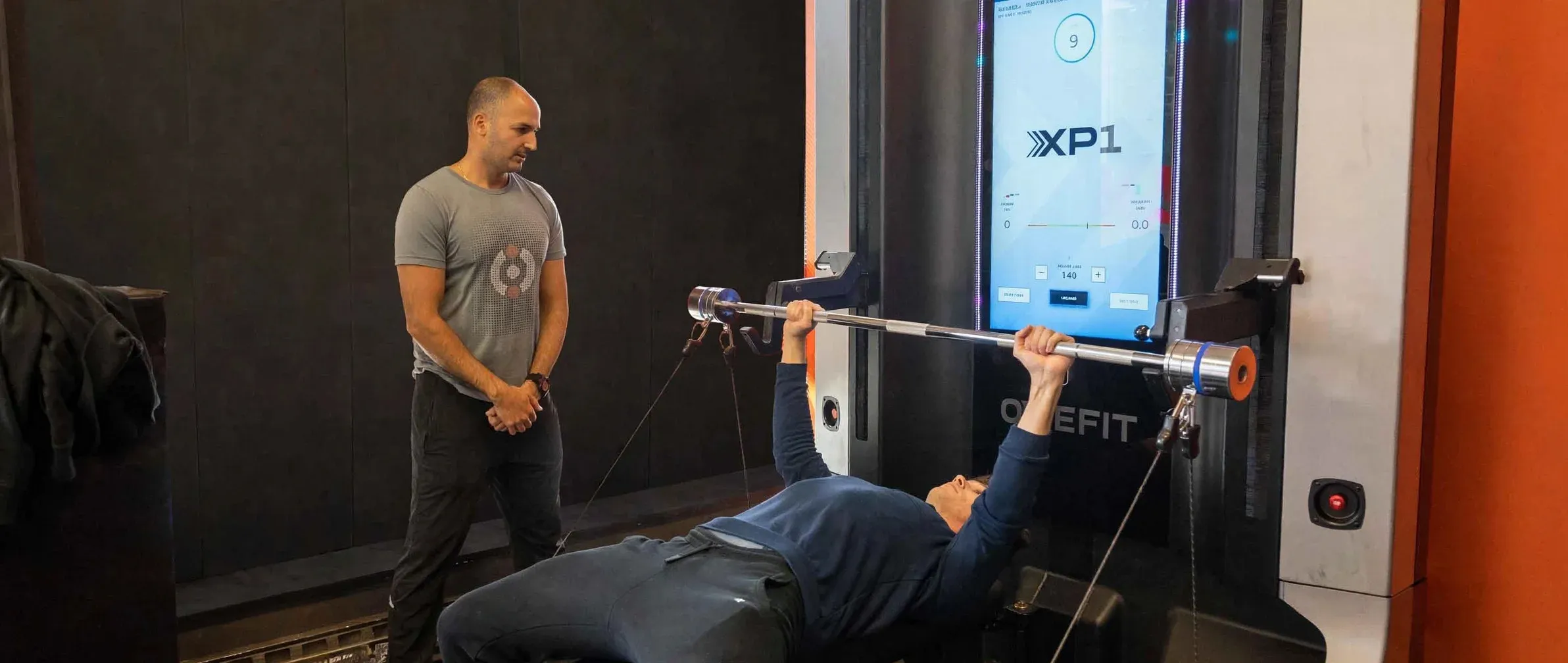 Kaeos co-owner coaching a client through a bench press on the OxeFit XP1